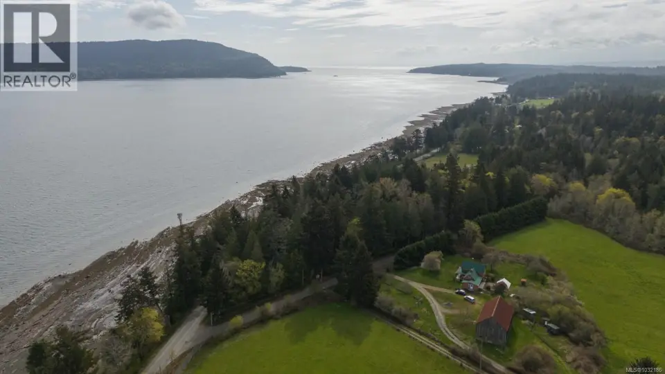 Expansive waterfront property featuring a main residence, an additional outbuilding with a red roof, and abundant mature trees