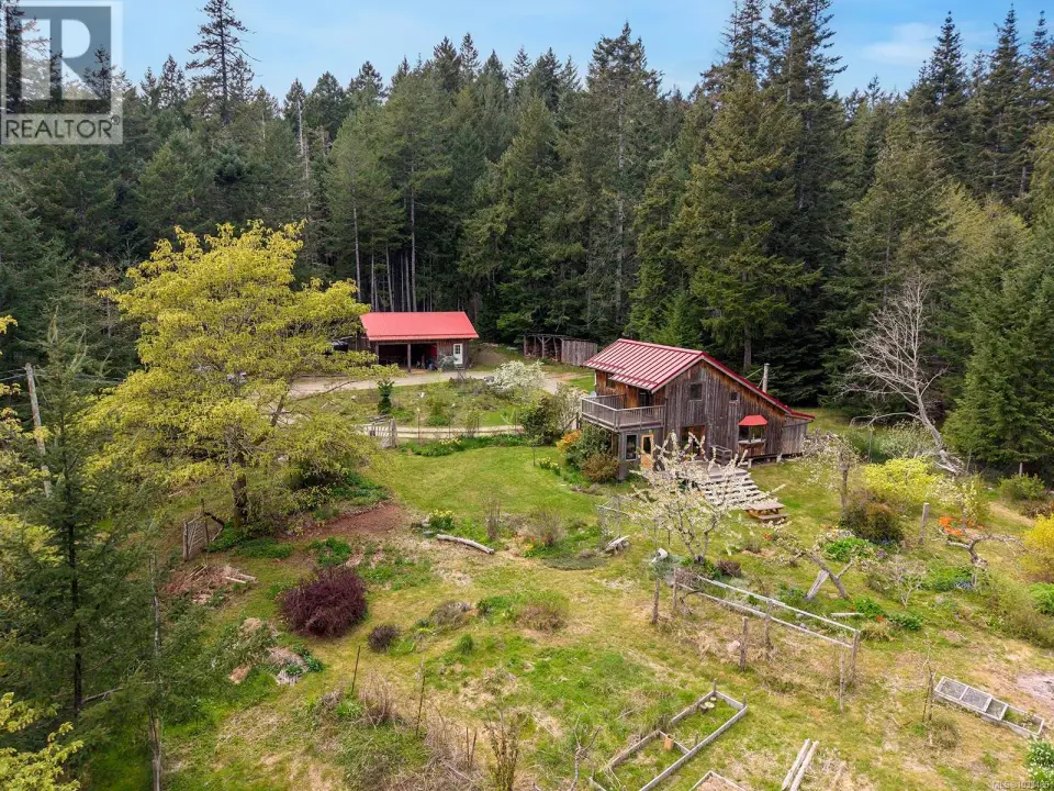 Wood-sided home with a red metal roof and an upper-level balcony, surrounded by mature trees