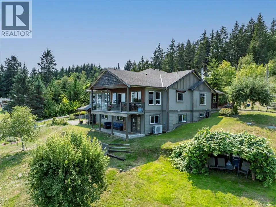 Modern two-story residence featuring a composite or fiber cement exterior in soft gray-blue tones, set on expansive grounds surrounded by mature evergreen and deciduous trees