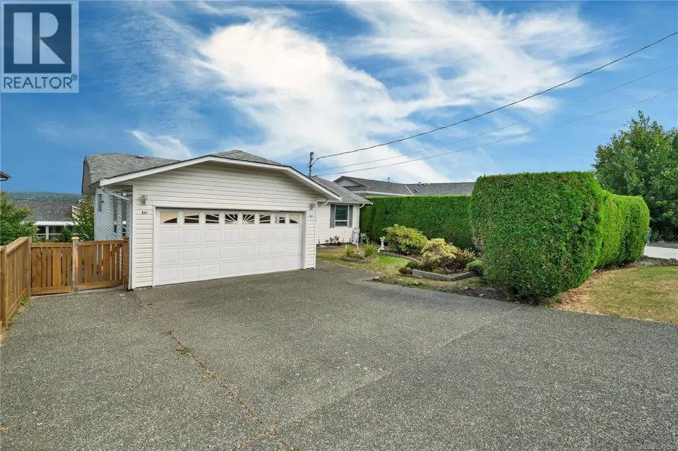 White siding exterior with a two-car garage, concrete driveway, and a natural wood fence